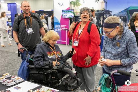 Attendees including special needs transport users react to a trade show booth at American Public Transit Association Trade show and Conference